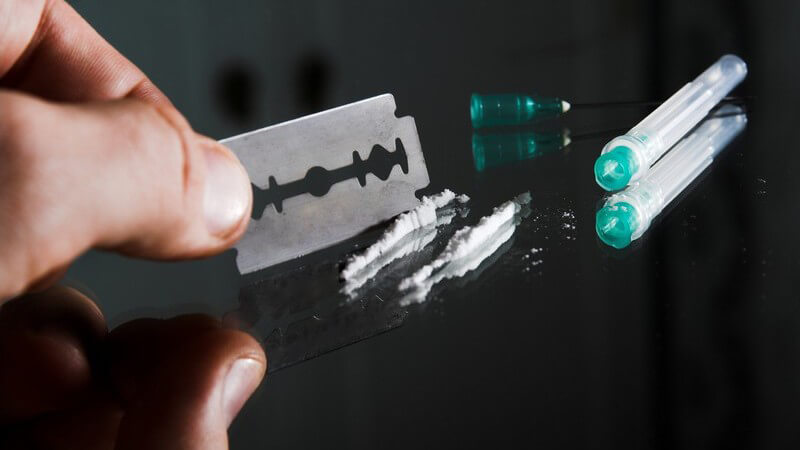 Drogen in Pulverform auf Glasplatte, daneben Spritze