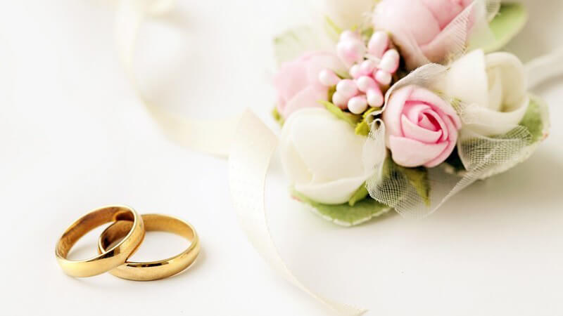 Zwei goldene Hochzeitsringe neben einem kleinen rosa-weißen Blumenstrauß