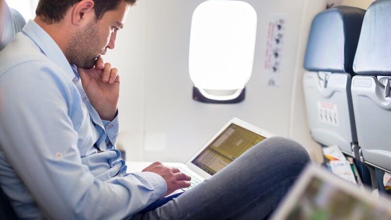 Geschäftsmann sitzt im Flugzeug und arbeitet am Laptop