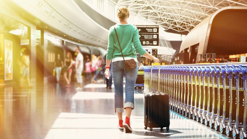 Frau mit grüner Strickjacke und roten Schuhen läuft mit einem Trolley durch den Flughafen