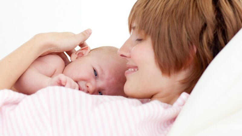 Junge Mutter mit Neugeborenem im Bett, weißer Hintergrund
