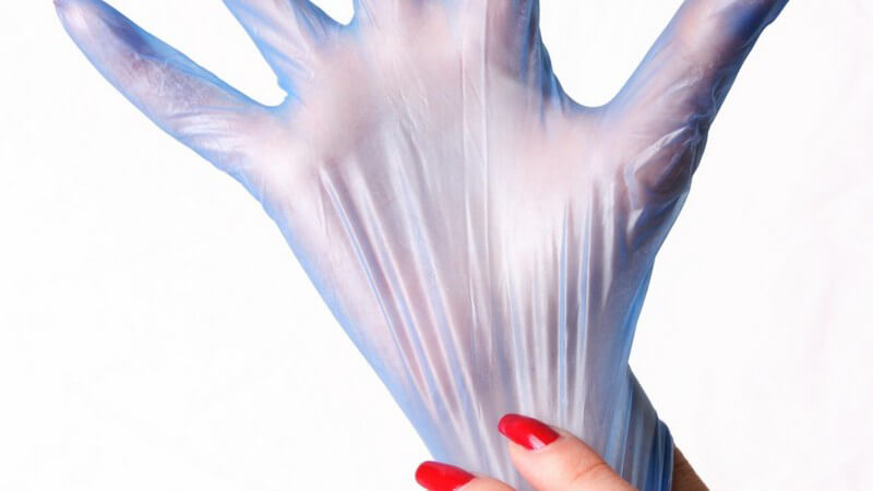 Frau mit rotlackierten Fingernägeln zieht sich einen Handschuh an