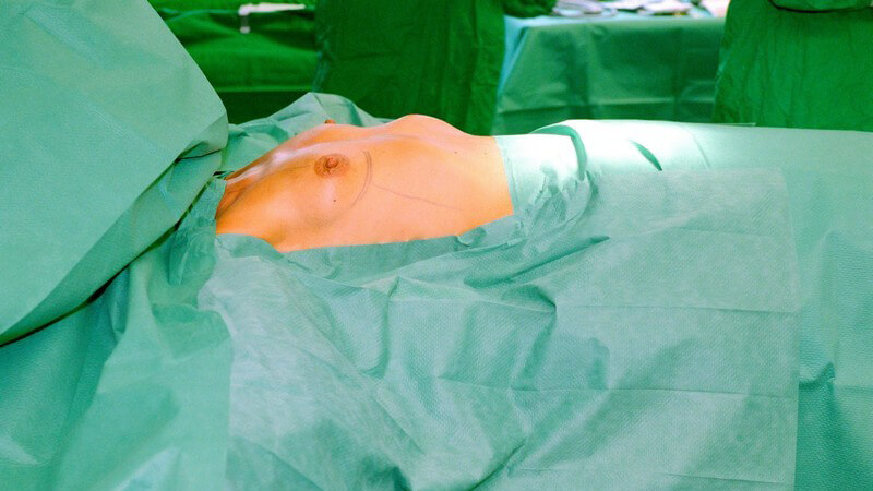 Patientin mit kleiner Brust auf Liege im Operationssaal, kurz vor Brustvergrößerung