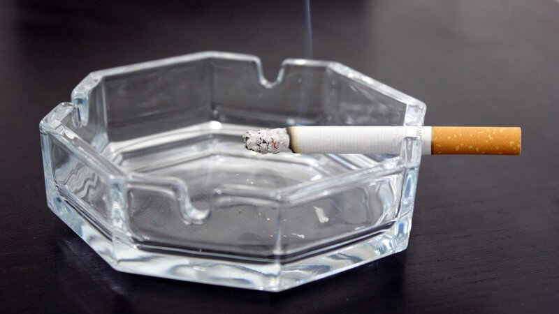 Glas Aschenbecher mit glühender Zigarette auf schwarzem Tisch