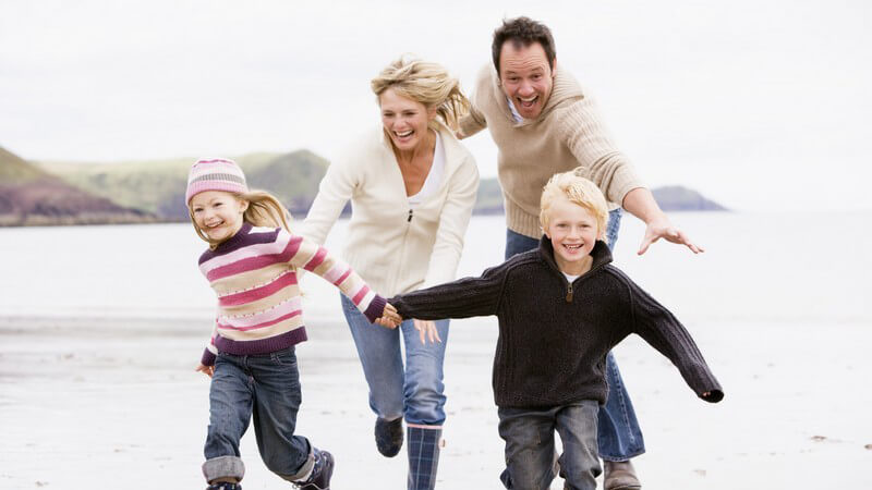 Junge Familie hält sich an den Händen und rennt lachend am Strand entlang