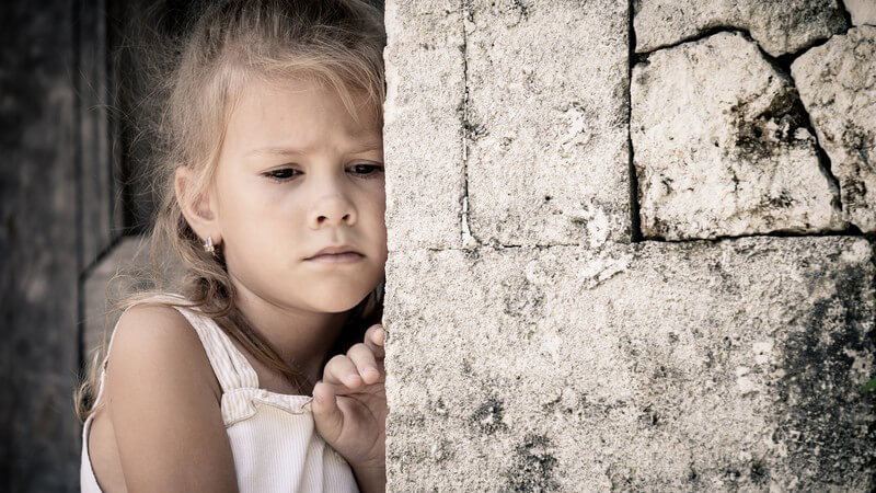 Kleines Mädchen steht traurig hinter einer alten Steinmauer