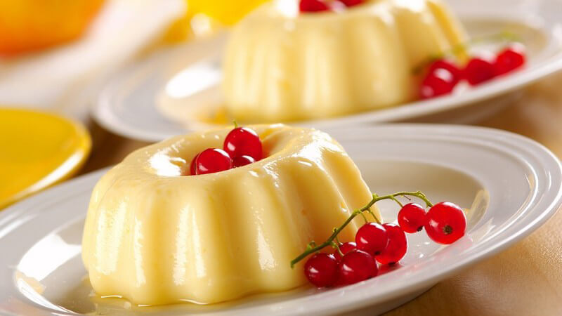 Zwei Portionen Vanillepudding mit Soße und roten Johannisbeeren auf weißen Tellern