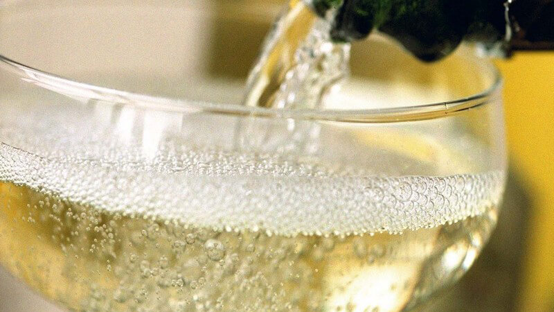 Nahaufnahme Hals der Champagnerflasche gießt Champagner in Champagnerglas vor gelbem, hellen Hintergrund