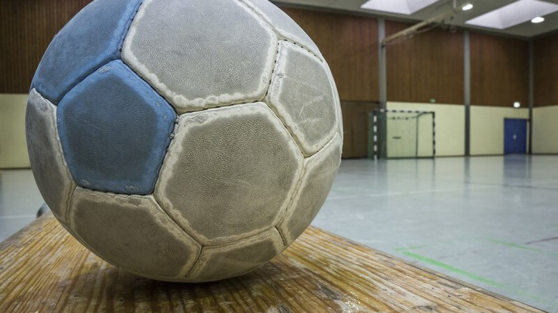Grau-blauer Handball liegt auf dem Boden einer Turnhalle