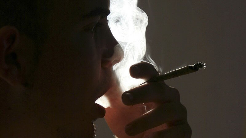 Mann raucht einen Joint und atmet viel Qualm aus
