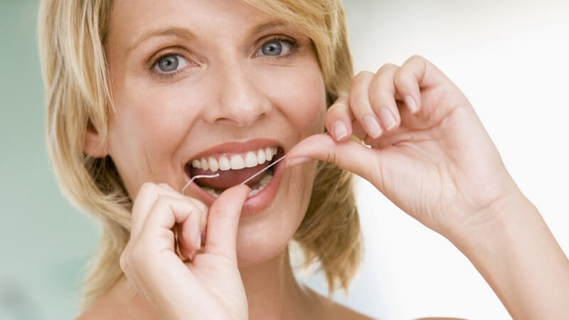 Blonde lächelnde Frau bei Mundhygiene, benutzt Zahnseide