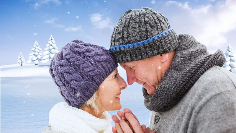 Reiferes Paar, Stirn an Stirn, lächelt sich an, Winterbild mit Schnee, Schals und Wollmützen