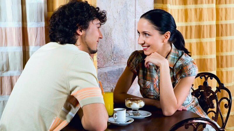 Schwarzhaariges Paar an Bistrotisch mit Kaffee, Dessert und Orangensaft