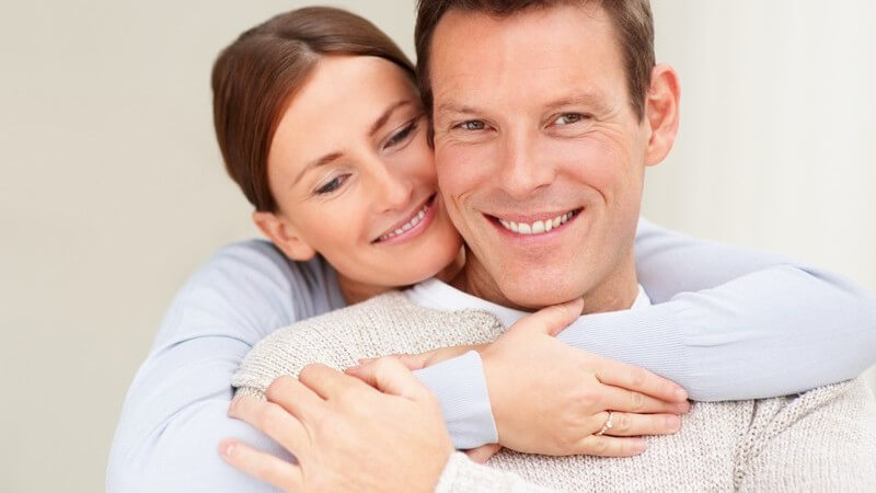 Frau umarmt ihren Mann von hinten, beide lächeln