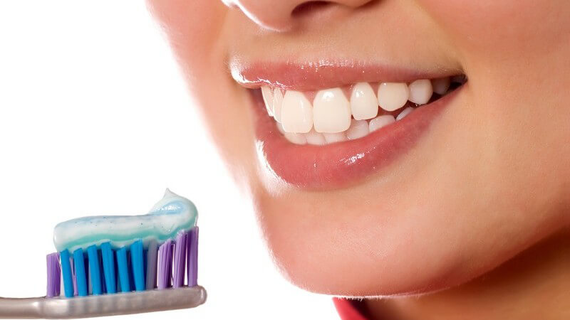 Lächelnder Frauenmund, Zahnbürste mit Zahnpasta davor