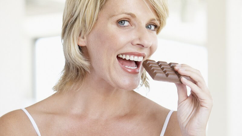Blonde Frau beißt fröhlich in Tafel Schokolade