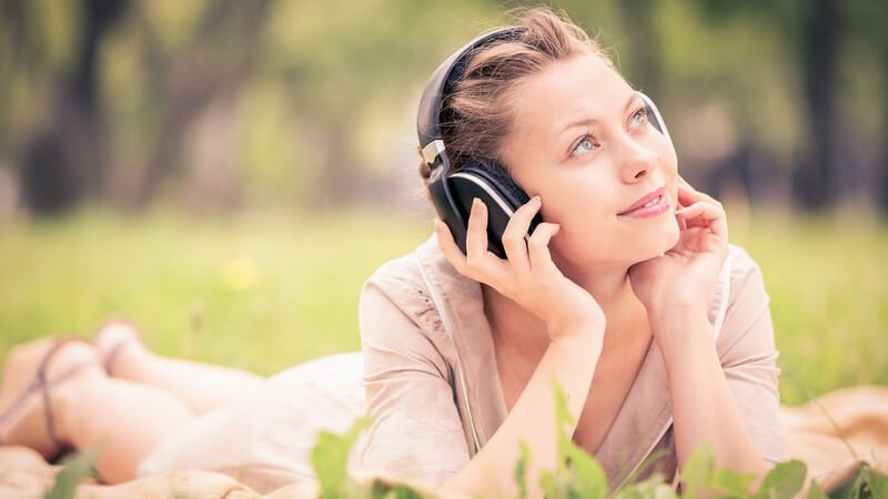 Junge Frau liegt auf einer Wiese im Park und hört Musik aus großen Kopfhörern