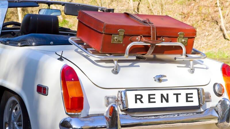 Weißes Oldtimer-Cariolet mit rotem Koffer und einem Kennzeichen mit der Aufschrift "RENTE"