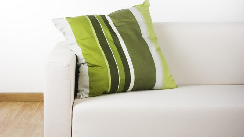 Stück einer weißen Couch mit grünem Kissen auf Holzboden