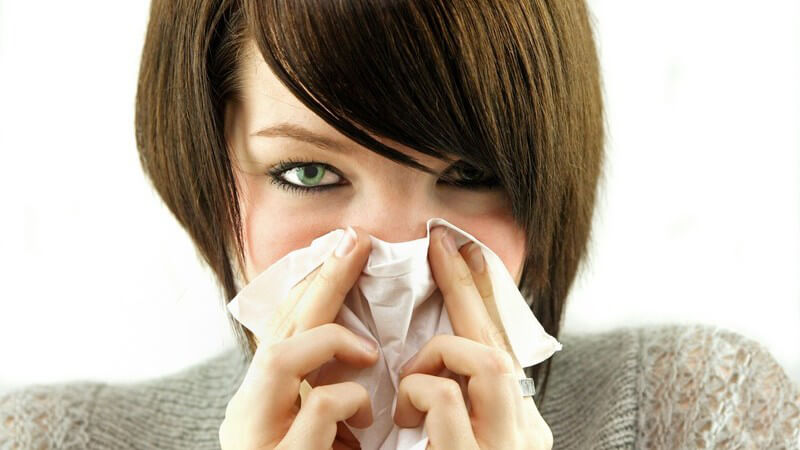 Junge Frau mit Erkältung putzt Nase mit Taschentuch