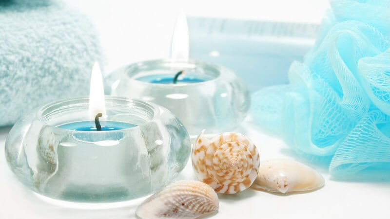 Gläserne Teelichthalter mit blauen Kerzen, Muscheln, blauer Badeschwamm