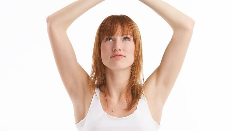 Rothaarige Frau in weißem Oberteil beim Yoga, die Hände über dem Kopf zugespitzt
