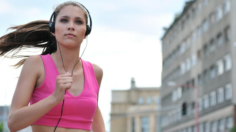 Junge Frau joggt in Stadt, hört Musik über Kopfhörer