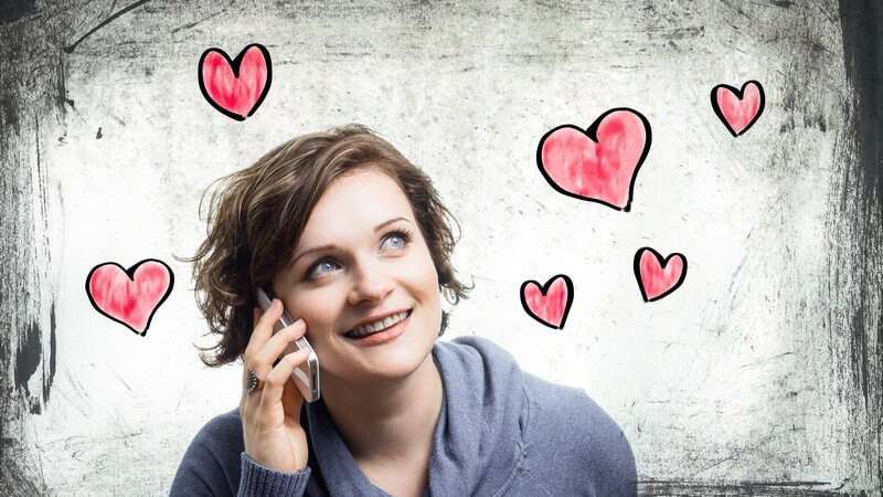 Verliebte junge Frau beim Telefonieren mit dem Smartphone, um sie herum viele rote, gemalte Herzchen (Fotomontage)