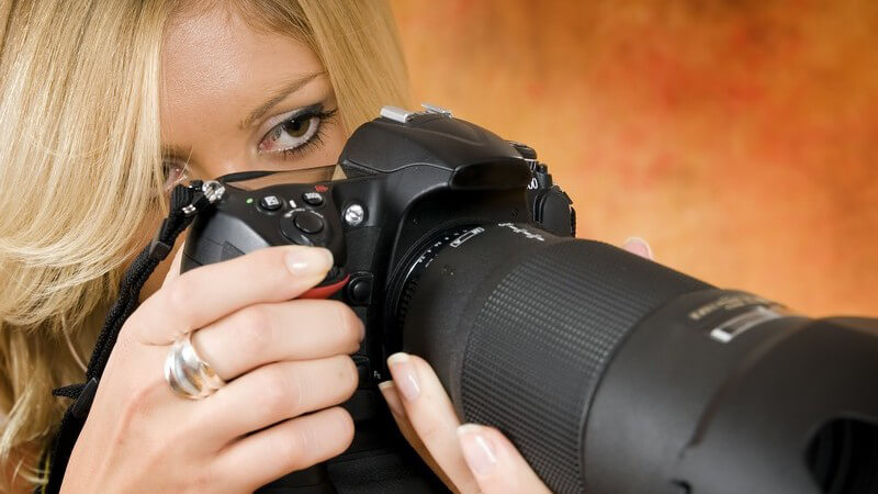 Junge Fotografin schaut durch professionelle Kamera