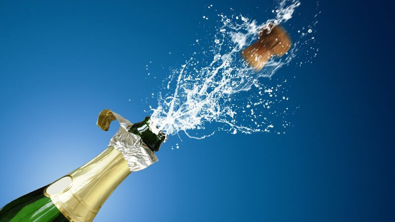 Korken springt aus Champagnerflasche vor blauem Hintergrund