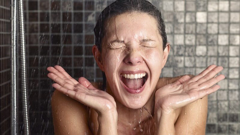 Frau mit aufgerissenem Mund und geschlossenen Augen unter der Dusche