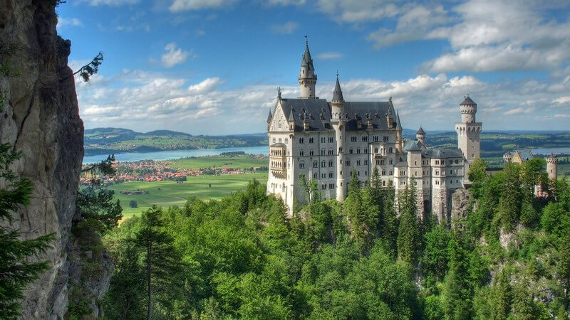Schloss Neuschwanstein auf waldigem Berg, blauer Himmel und Wolken