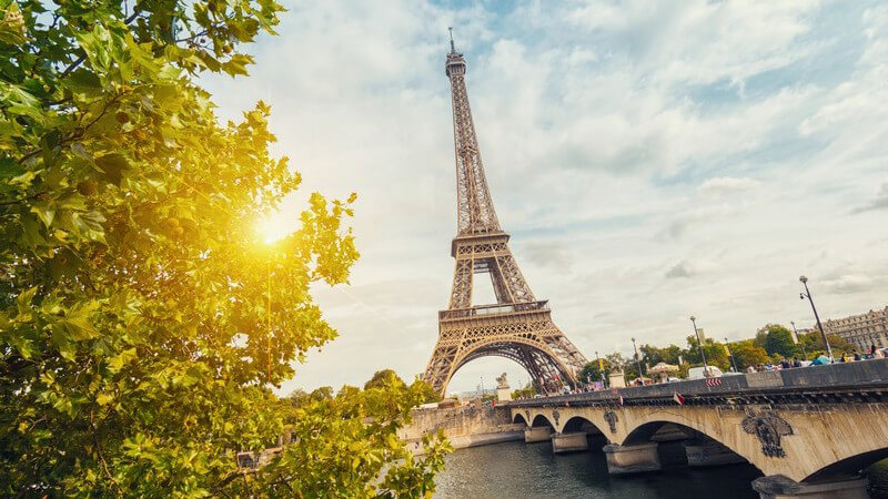 Grüner Baum, Eiffelturm und Brücke über die Seine bei Sonnenuntergang in Paris