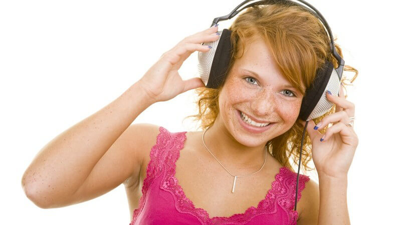 Junge, rothaarige Frau hält ihre großen Kopfhörer an Ohren und lacht