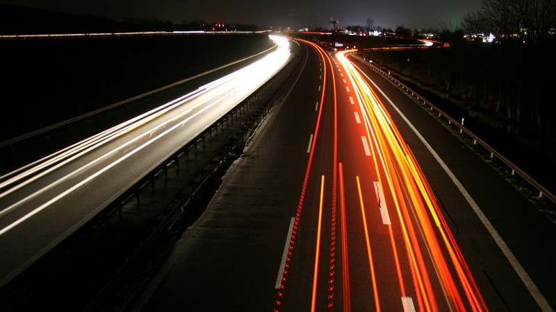 Autobahn bei Nacht von oben: fahrende Autos hinterlassen leuchtende Lichtstreifen