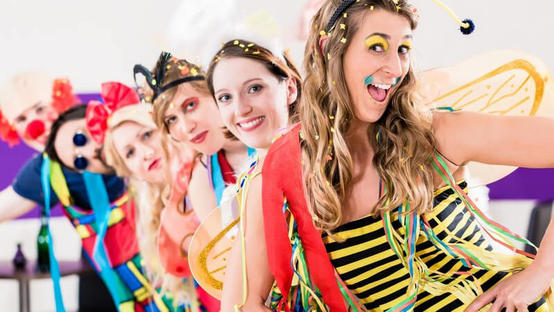 Junge Leute in Karnevalskostümen wie Biene und Clown stehen in einer Reihe