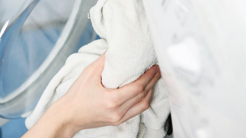 Weibliche Hand legt weiße Handtücher in Waschmaschine zum Waschen