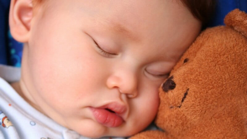 Gesicht eines Säuglings, schläft neben seinem Teddybären