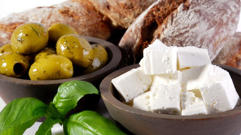 Nahaufnahme frisches Brot, Oliven, Fetakäse und Basilikumblätter auf weißem Hintergrund