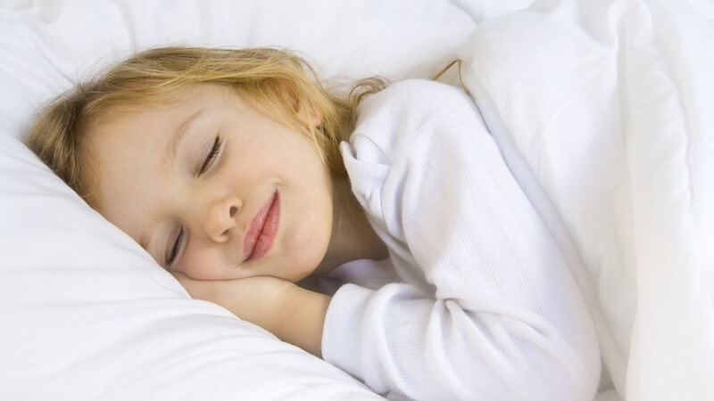 Kleines Mädchen liegt lächelnd im Bett und schläft