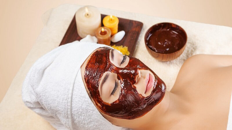 Frau mit Handtuch im Haar lässt eine Schokoladen-Gesichtsmaske einwirken