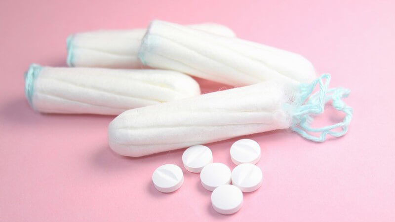 Tampons und Schmerztabletten auf rosanem Hintergrund Menstruationsschmerzen