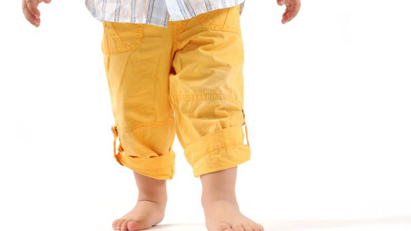 Unterkörper eines Kleinkinds, nackte Füße, weißer Hintergrund