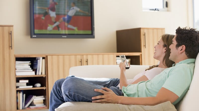 Seitenansicht junges Paar sitzt auf Couch und schaut Fußball im Fernsehen