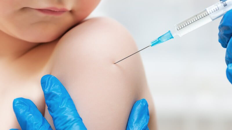 Junge bekommt zur Impfung eine Spritze in den Oberarm, der Arzt trägt blaue Handschuhe