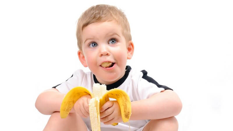 Kleinkind isst Banane und schaut nach oben