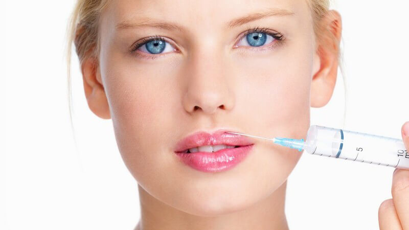 Junge Frau hält eine Botox Spritze an ihre Lippen