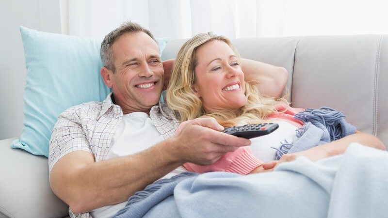 Älteres Paar liegt eingekuschelt auf der Couch und guckt Fernsehen