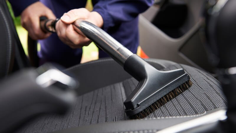 Mann saugt einen Sitz im Auto mit einem Autostaubsauger