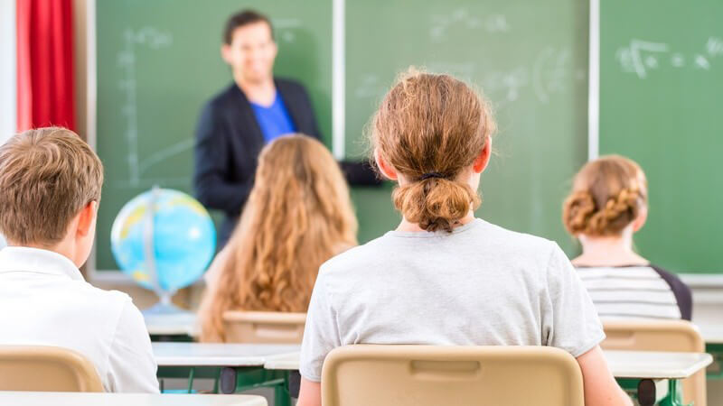 Vier Schüler sitzen im Klassenzimmer und blicken zum Lehrer an die Tafel